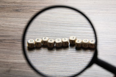 Photo of Word Depression made of wooden cubes on table, view through magnifying glass