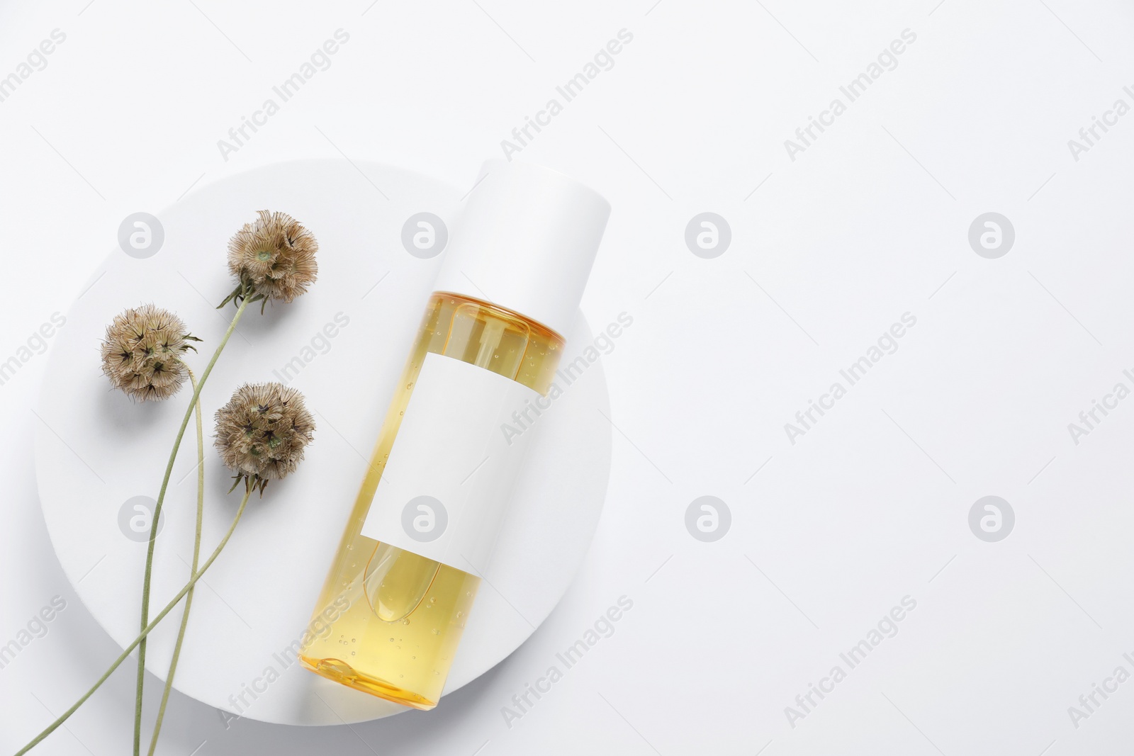 Photo of Bottle of cosmetic product, dried flowers and round podium on white background, top view. Space for text