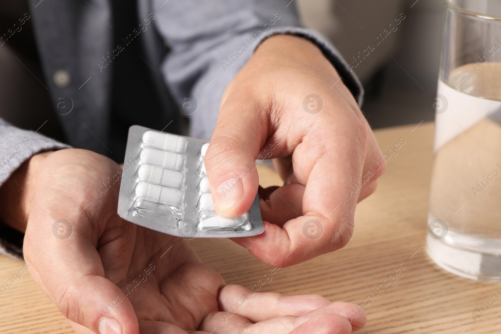 Photo of Man taking pill out from blister pack at wooden table, closeup