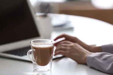 Woman with cup of coffee and laptop at table, closeup