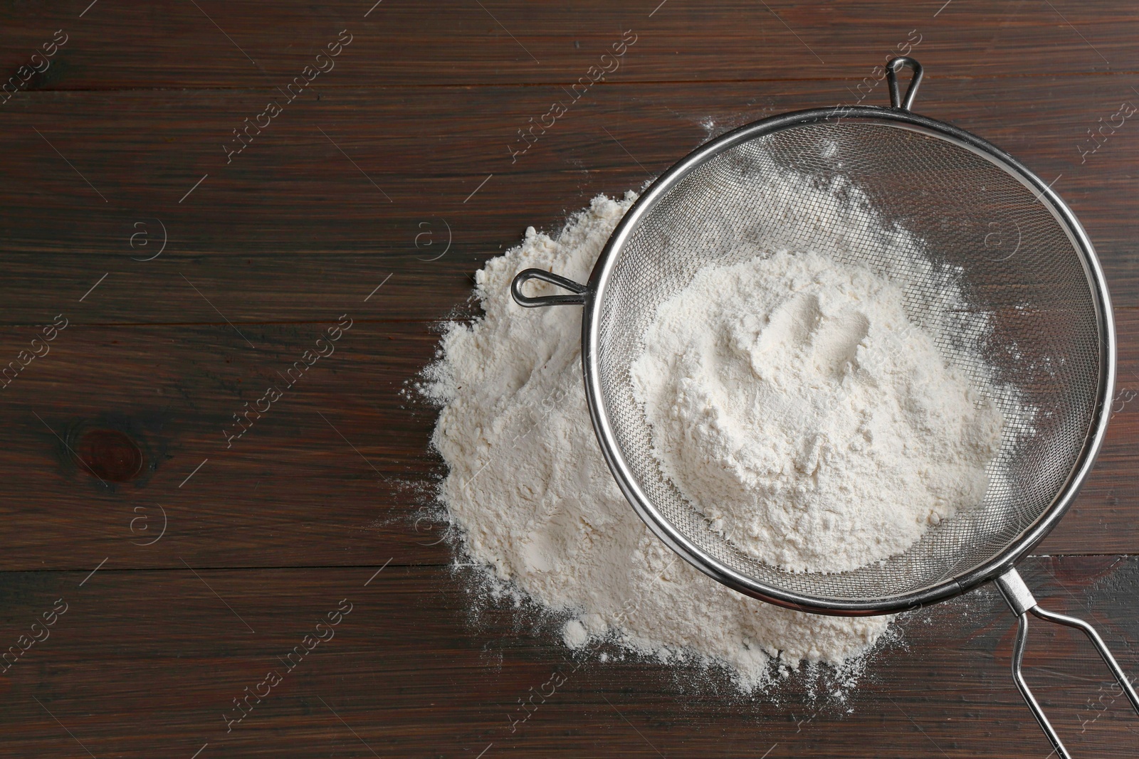 Photo of Metal sieve with flour on wooden table, top view. Space for text