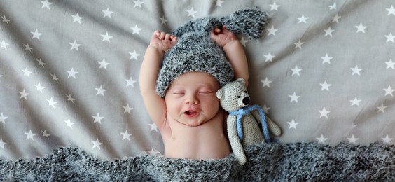 Image of Cute newborn baby in warm hat with toy sleeping on bed, top view. Banner design
