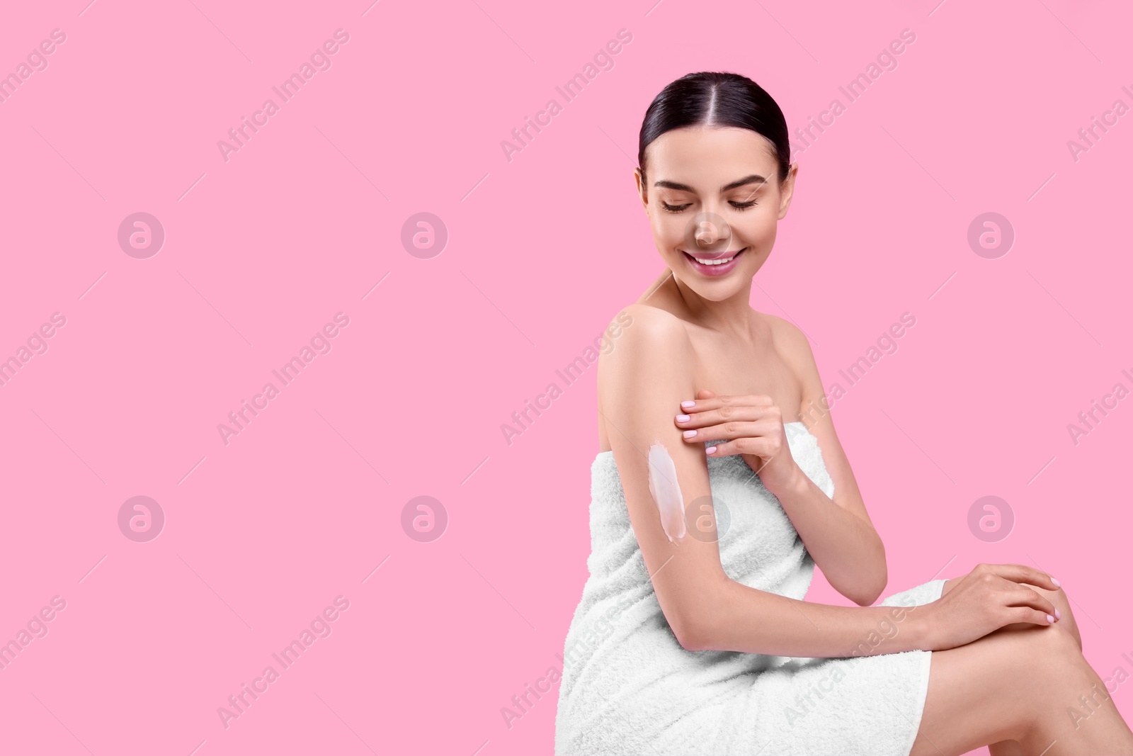 Photo of Beautiful woman with smear of body cream on her arm against pink background, space for text