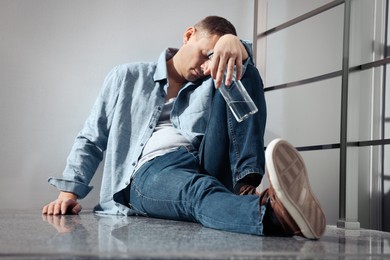 Addicted drunk man with alcoholic drink on floor indoors