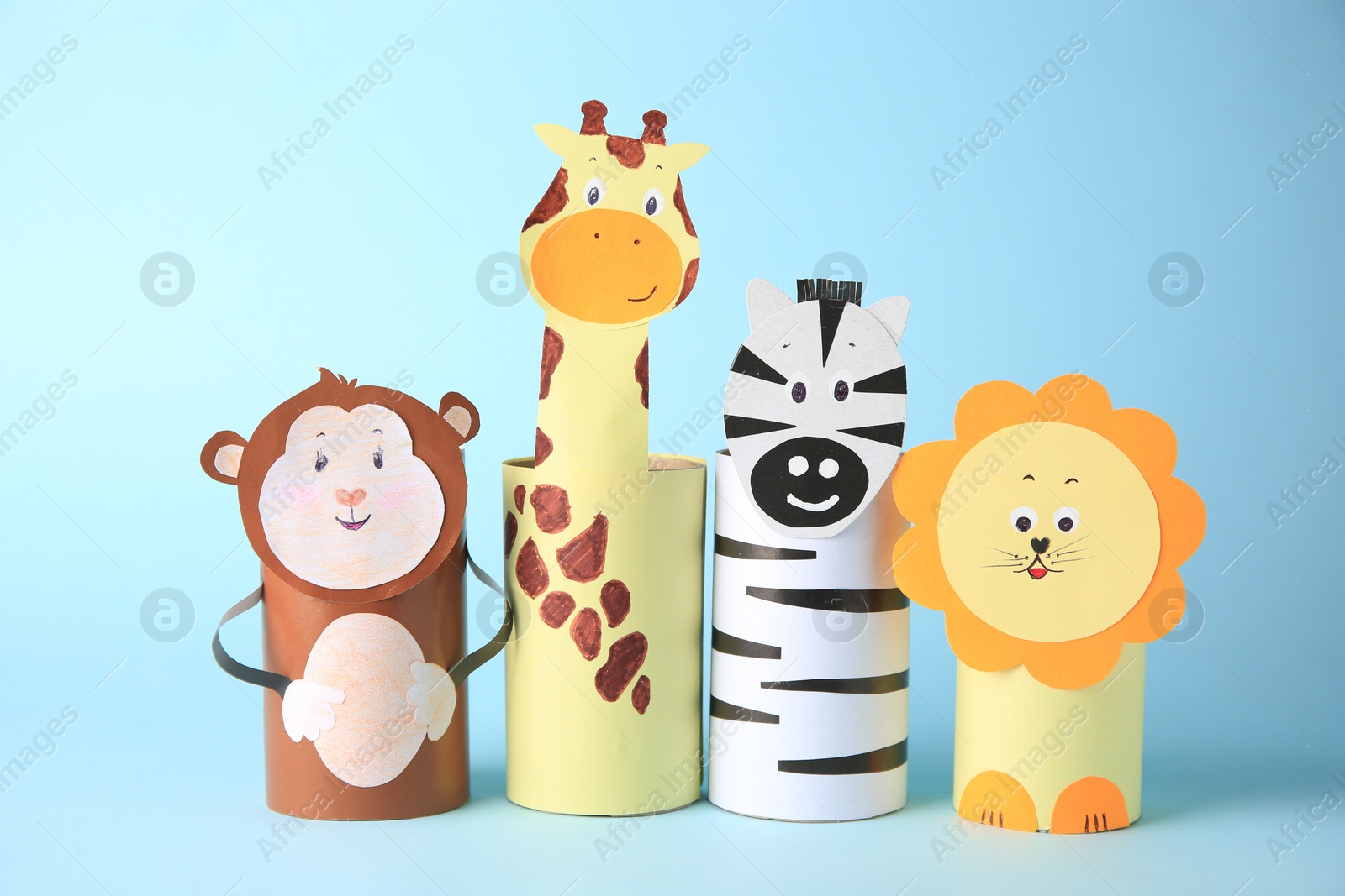 Photo of Toy monkey, giraffe, lion and zebra made from toilet paper hubs on light blue background. Children's handmade ideas