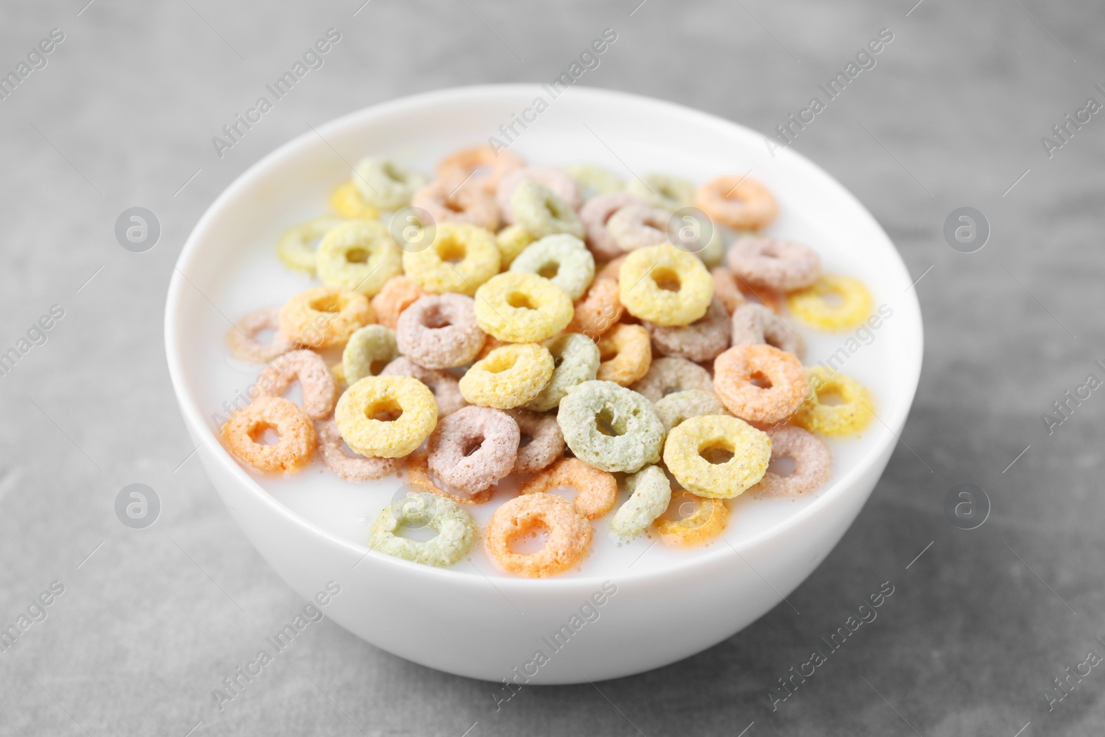 Photo of Tasty colorful cereal rings and milk in bowl on grey table, closeup