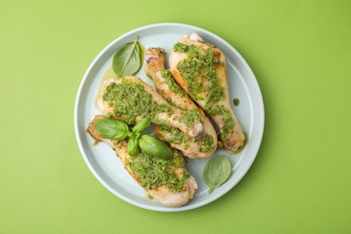 Delicious fried chicken drumsticks with pesto sauce and basil on green table, top view