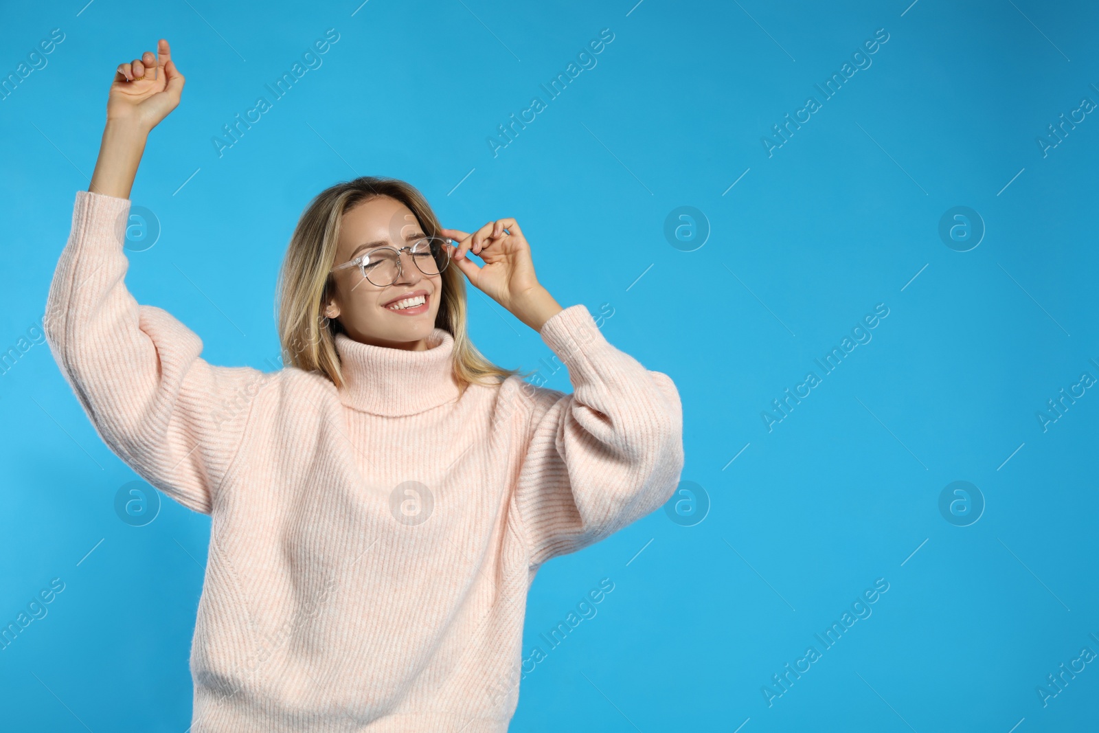 Photo of Beautiful young woman wearing knitted sweater on light blue background. Space for text