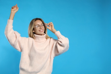 Beautiful young woman wearing knitted sweater on light blue background. Space for text