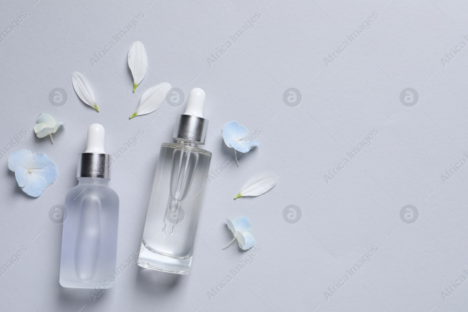 Photo of Bottles of cosmetic serums and beautiful flowers on light grey background, flat lay. Space for text
