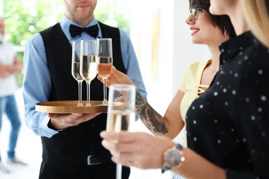 Photo of Waiter serving champagne to women at exhibition in art gallery