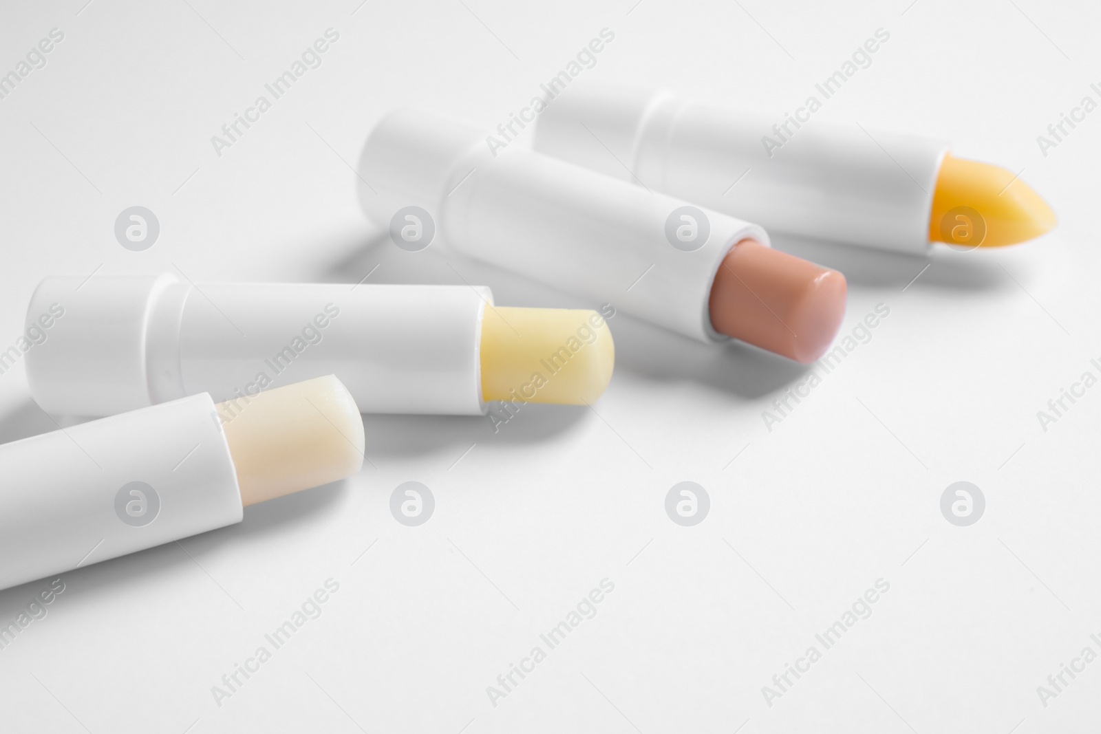 Photo of Different open hygienic lipsticks on white background