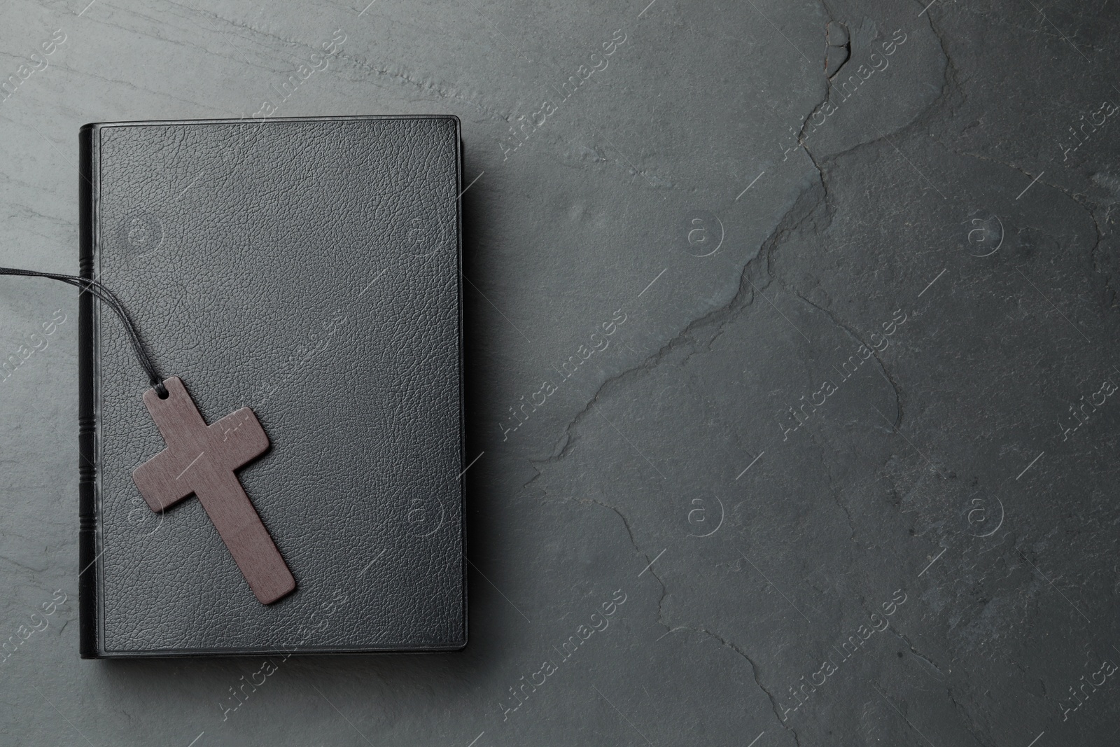 Photo of Wooden Christian cross and Bible on black table, top view. Space for text