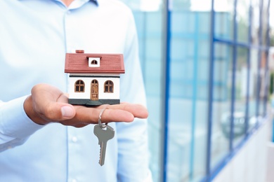 Real estate agent holding house model and key on blurred background