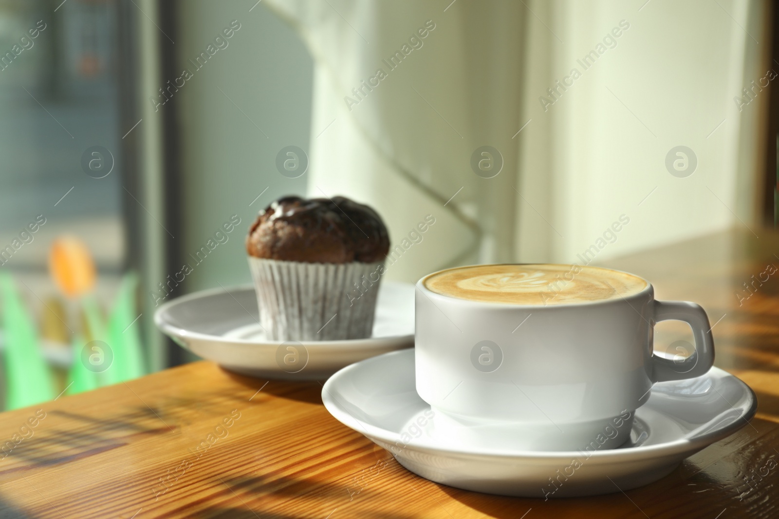 Photo of Cup of fresh aromatic coffee and cupcake at table in cafe