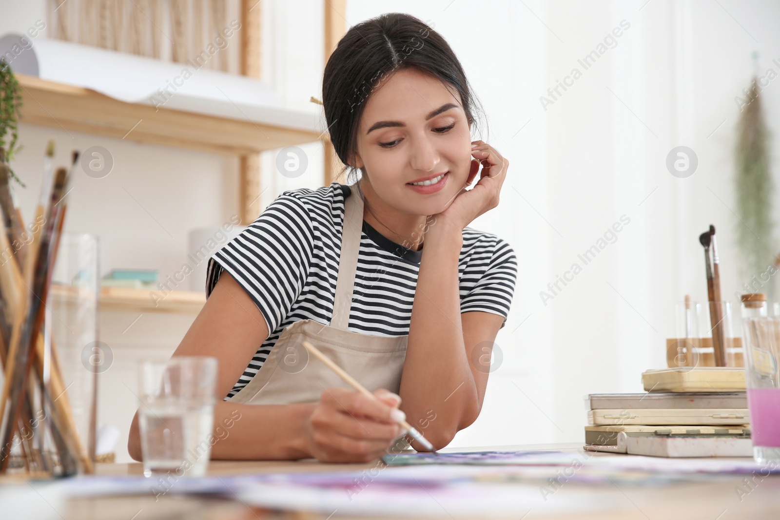 Photo of Young woman drawing with brush at table indoors