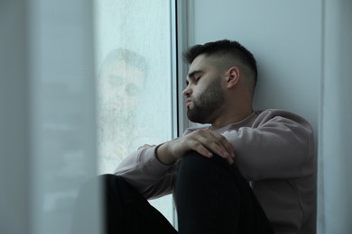 Photo of Sad man sitting near window at home