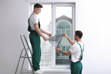 Professional workers tinting window with foil indoors