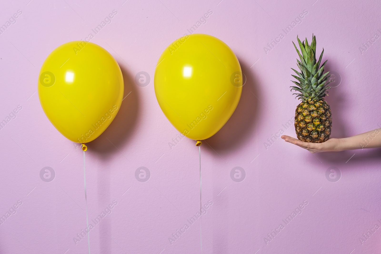 Photo of Woman holding pineapple near yellow balloons on color background