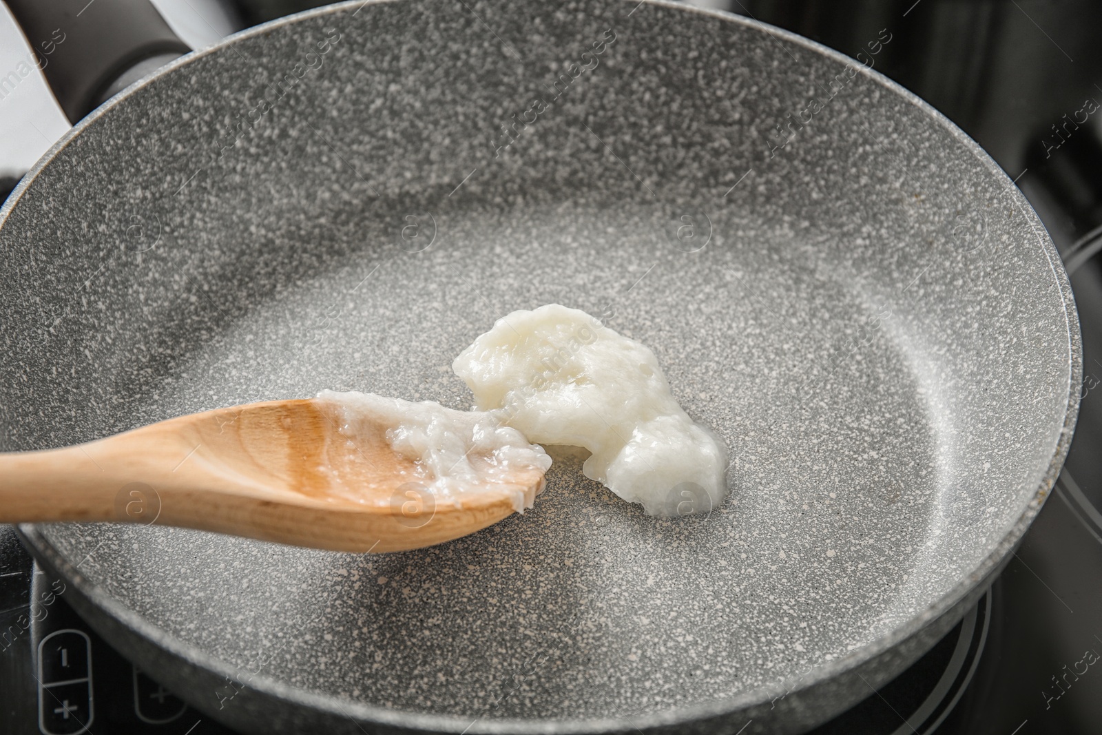 Photo of Wooden spoon with coconut oil in frying pan. Healthy cooking