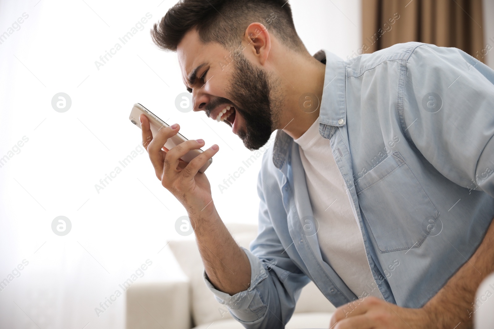 Photo of Emotional young man talking on mobile phone at home. Hate concept