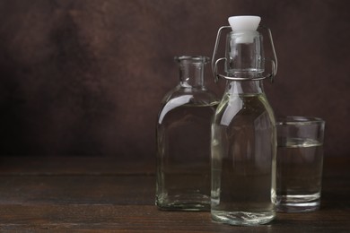 Vinegar in bottles and glass on wooden table, space for text