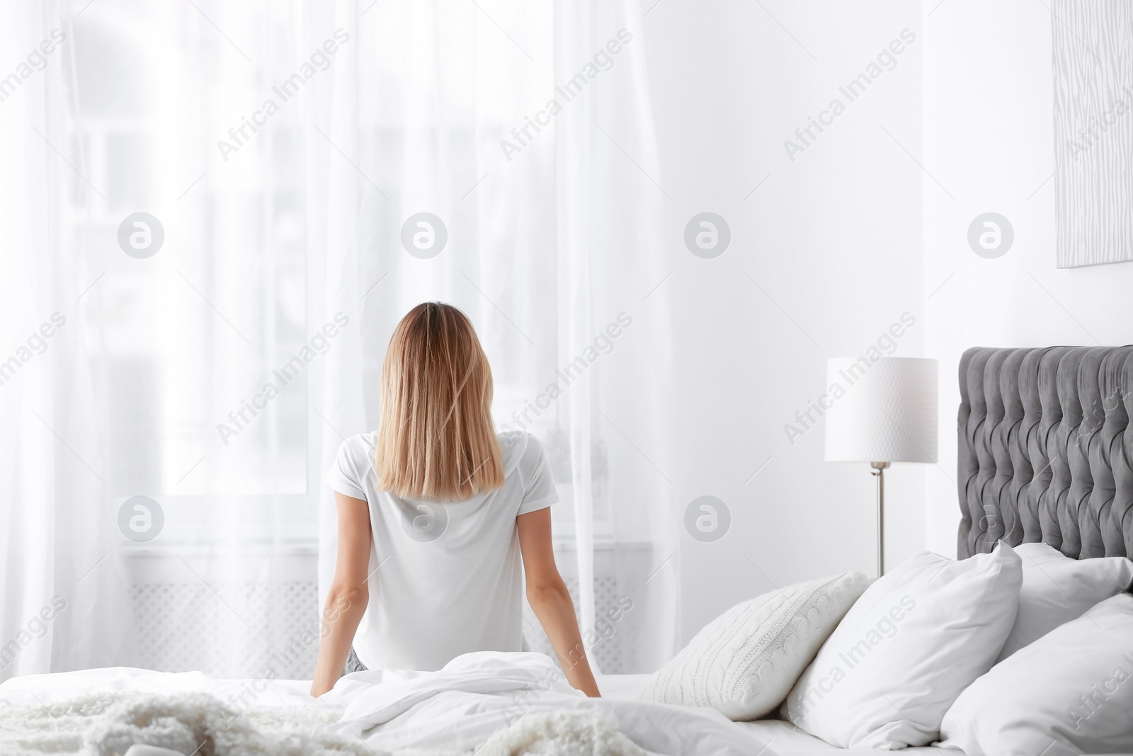 Photo of Young beautiful woman sitting on bed after sleeping at home
