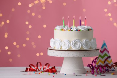 Photo of Delicious birthday cake and party decor on white wooden table against blurred festive lights, space for text
