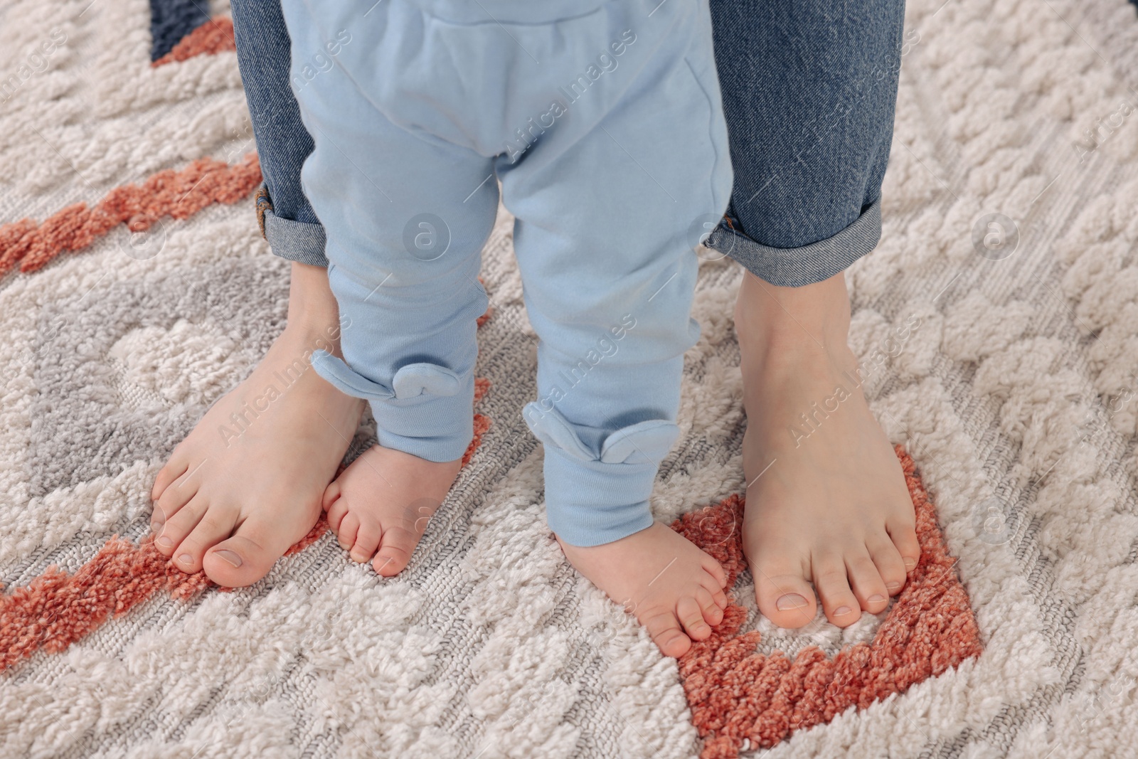 Photo of Mother supporting her baby son while he learning to walk on carpet, closeup