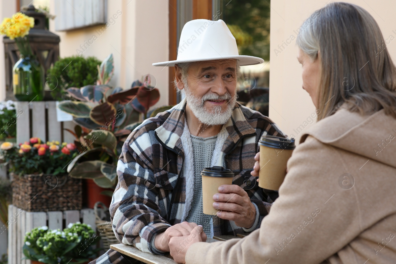 Photo of Affectionate senior couple sitting in outdoor cafe and drinking coffee, space for text