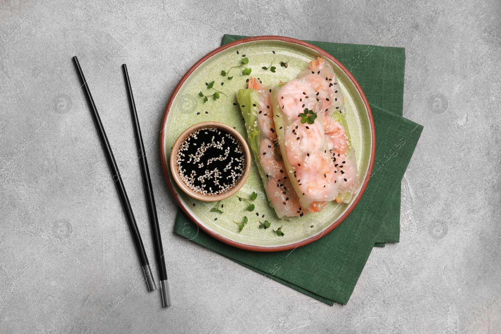 Photo of Tasty spring rolls served with soy sauce on grey textured table, flat lay