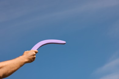 Man throwing boomerang against blue sky, closeup. Space for text