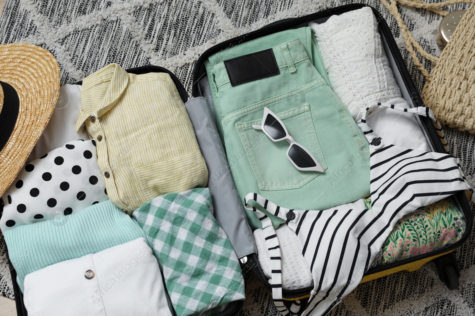 Photo of Open suitcase with summer clothes and accessories on floor, above view