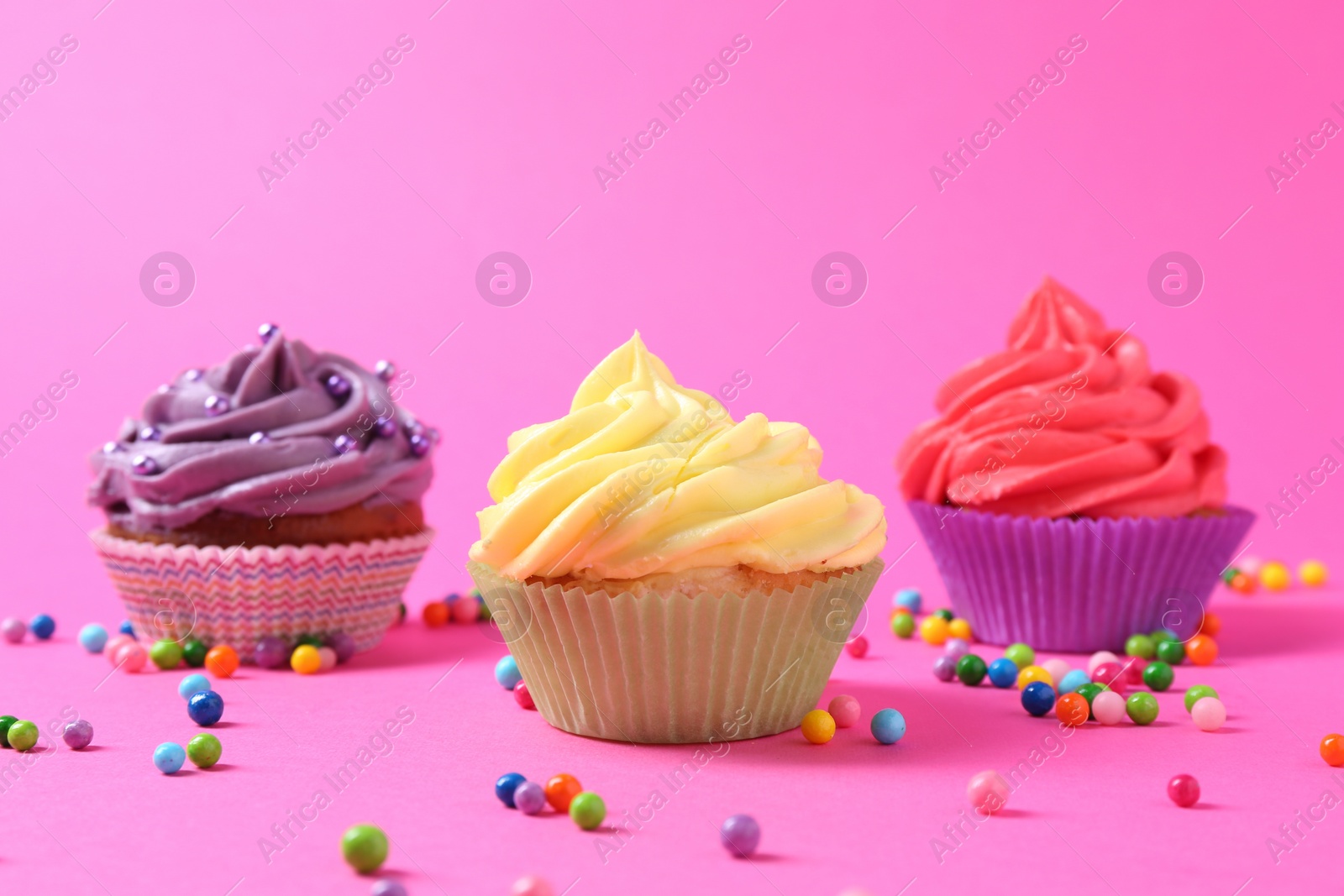 Photo of Delicious cupcakes with bright cream and sprinkles on pink background