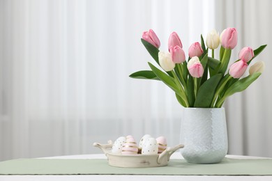 Easter decorations. Bouquet of tulips and painted eggs on white table indoors. Space for text