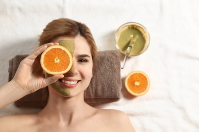 Woman with mask on face and cut orange relaxing in spa salon, top view. Space for text