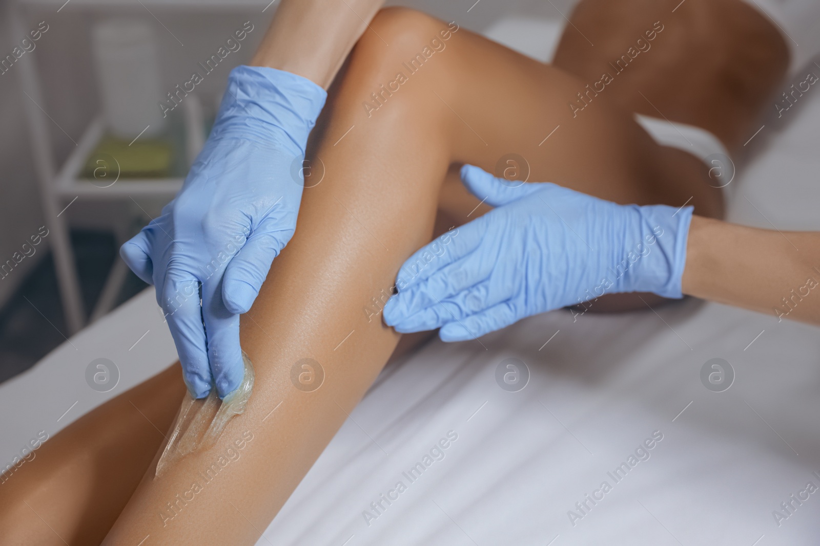 Photo of Young woman undergoing hair removal procedure on legs with sugaring paste in salon, closeup