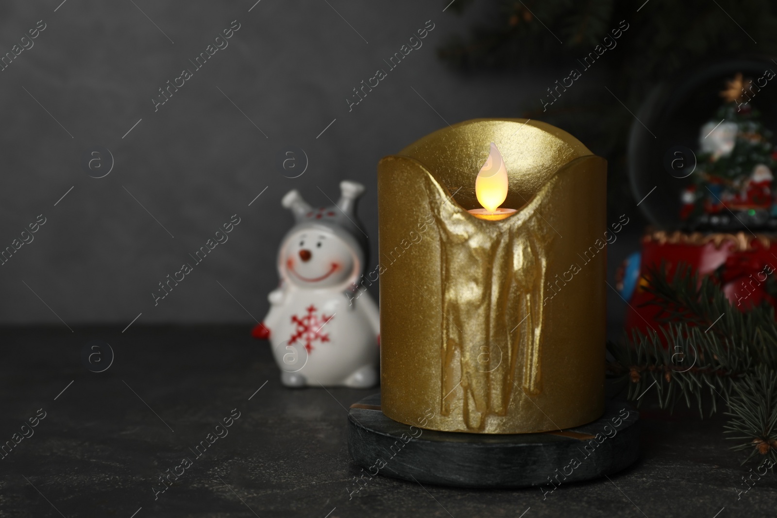 Photo of Golden LED candle and Christmas decor on black table. Space for text