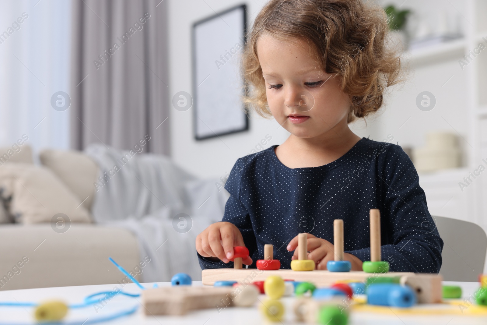 Photo of Motor skills development. Little girl playing with stacking and counting game at table indoors