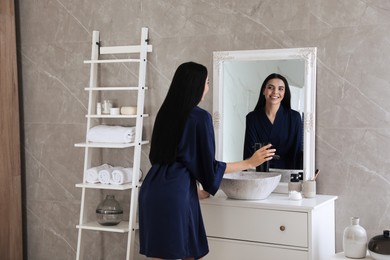Photo of Beautiful young woman looking at herself in bathroom mirror