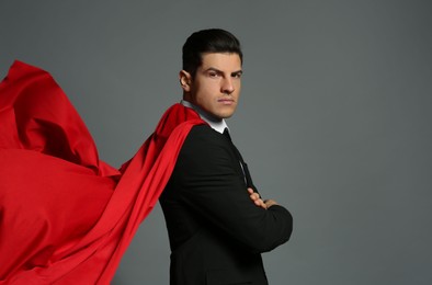 Businessman wearing superhero cape on grey background