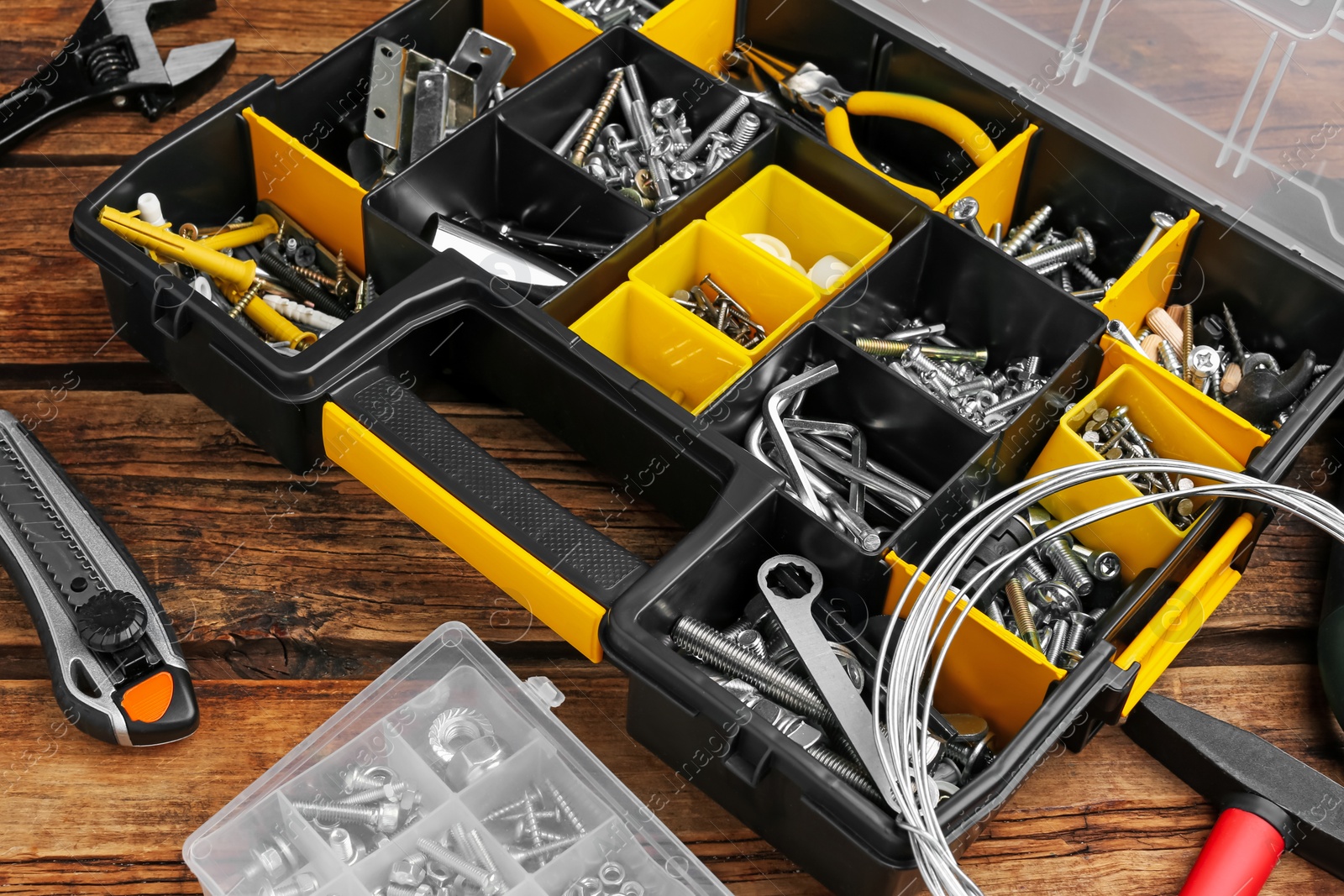 Photo of Plastic box with different bolts, nuts and tools on wooden table