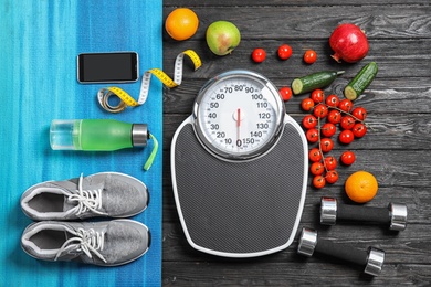 Flat lay composition with scales, healthy food and sport equipment on wooden background. Weight loss