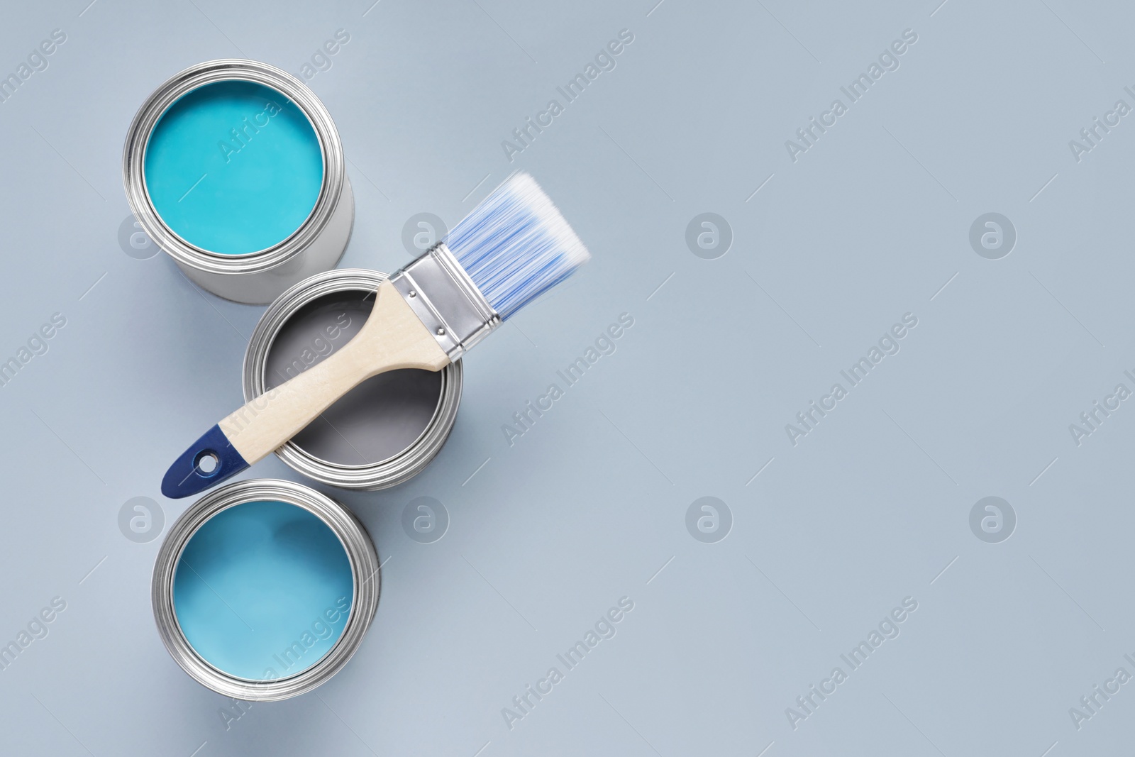 Photo of Cans with different paints and brush on light background, flat lay. Space for text