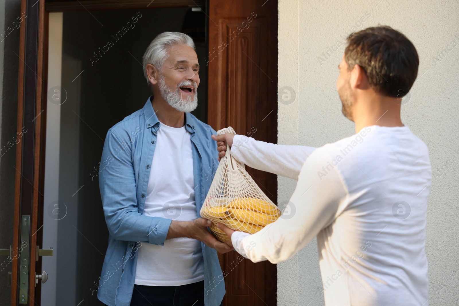 Photo of Man with net bag of products helping his senior neighbour outdoors