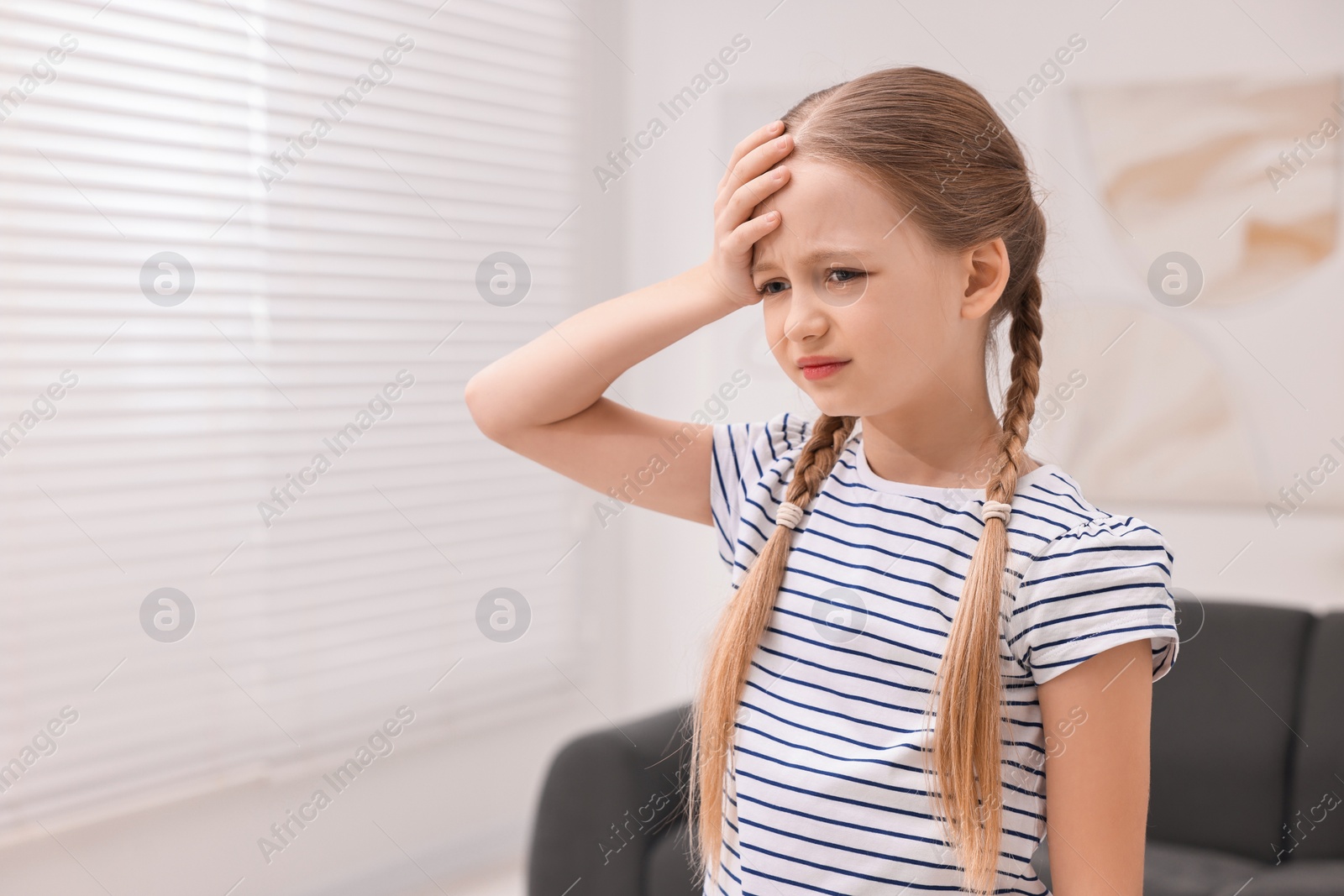 Photo of Little girl suffering from headache at home. Space for text