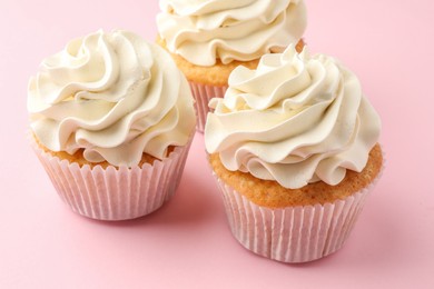 Photo of Tasty vanilla cupcakes with cream on pink table, closeup