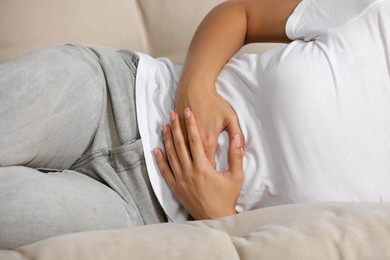 Photo of Young woman suffering from menstrual pain on sofa, closeup