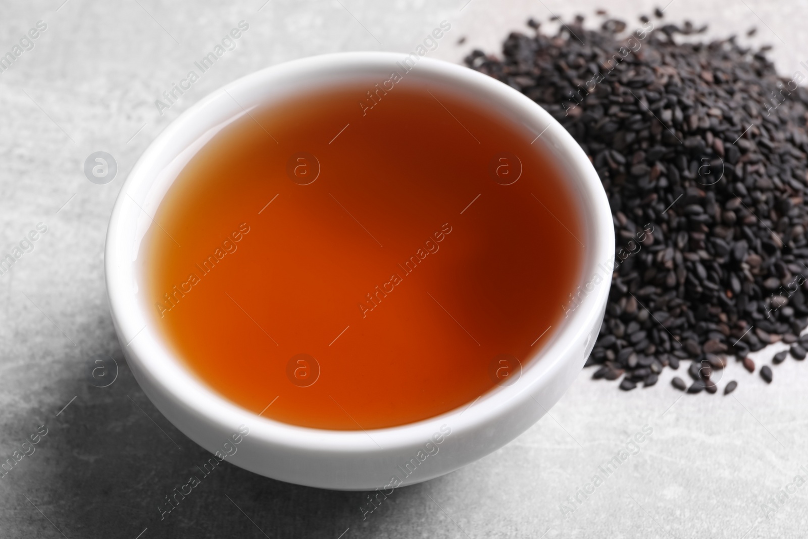 Photo of Fresh oil in bowl and black sesame seeds on grey table, closeup