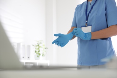 Photo of Doctor putting on medical gloves in office, closeup. Space for text